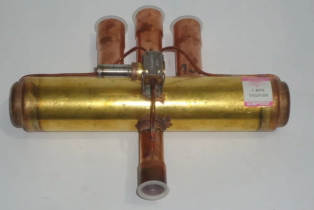 Daikin 4-Wege Ventil mit zwei Kupferrohren und einem zentralen Verbindungsteil. Die Oberfläche ist leicht oxidiert, was auf eine Nutzung hindeutet.